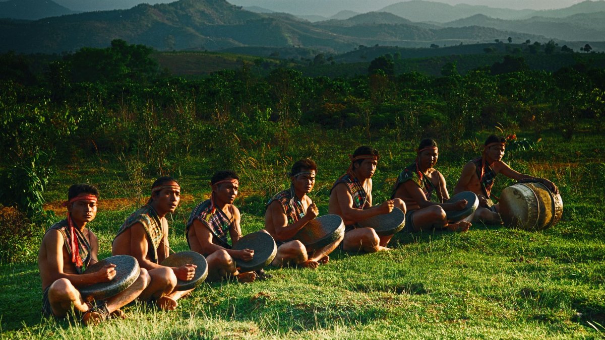 Group of men playing traditional drums in a scenic hilly landscape during the day.