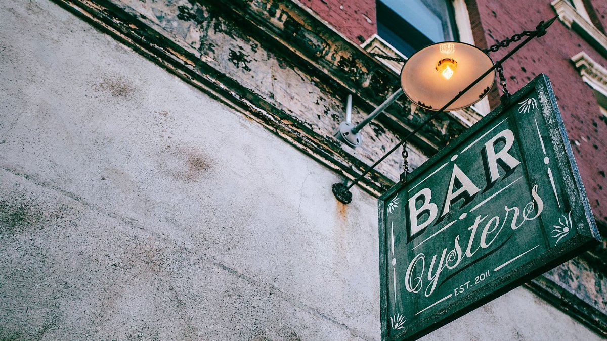 From below of rectangular shaped signboard with Bar and Oysters titles under lamp on aged wall in city