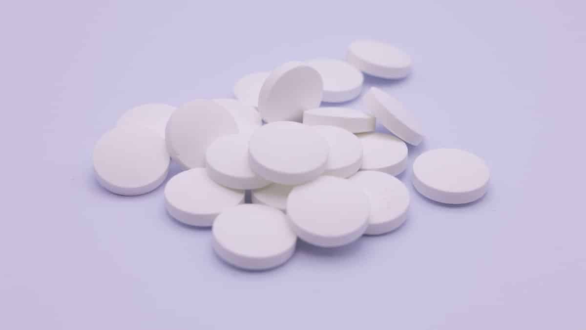 Assorted white tablets stacked on a soft purple surface, symbolizing medication and healthcare.