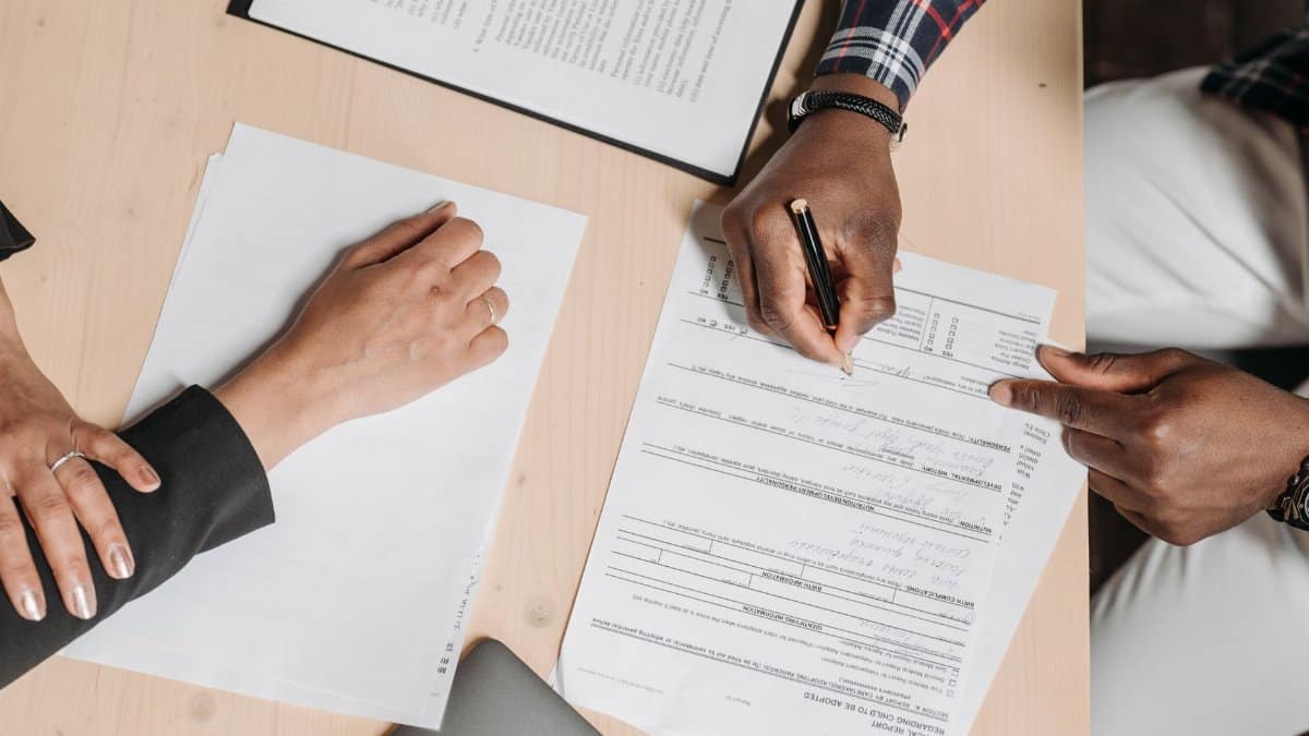 Close-up of two people signing documents at an office desk, depicting business collaboration.