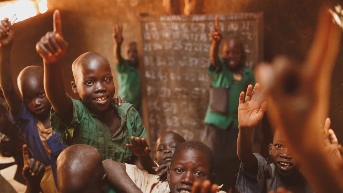 Young students in Kitgum, Uganda, enthusiastically participate in class, raising their hands with smiles.
