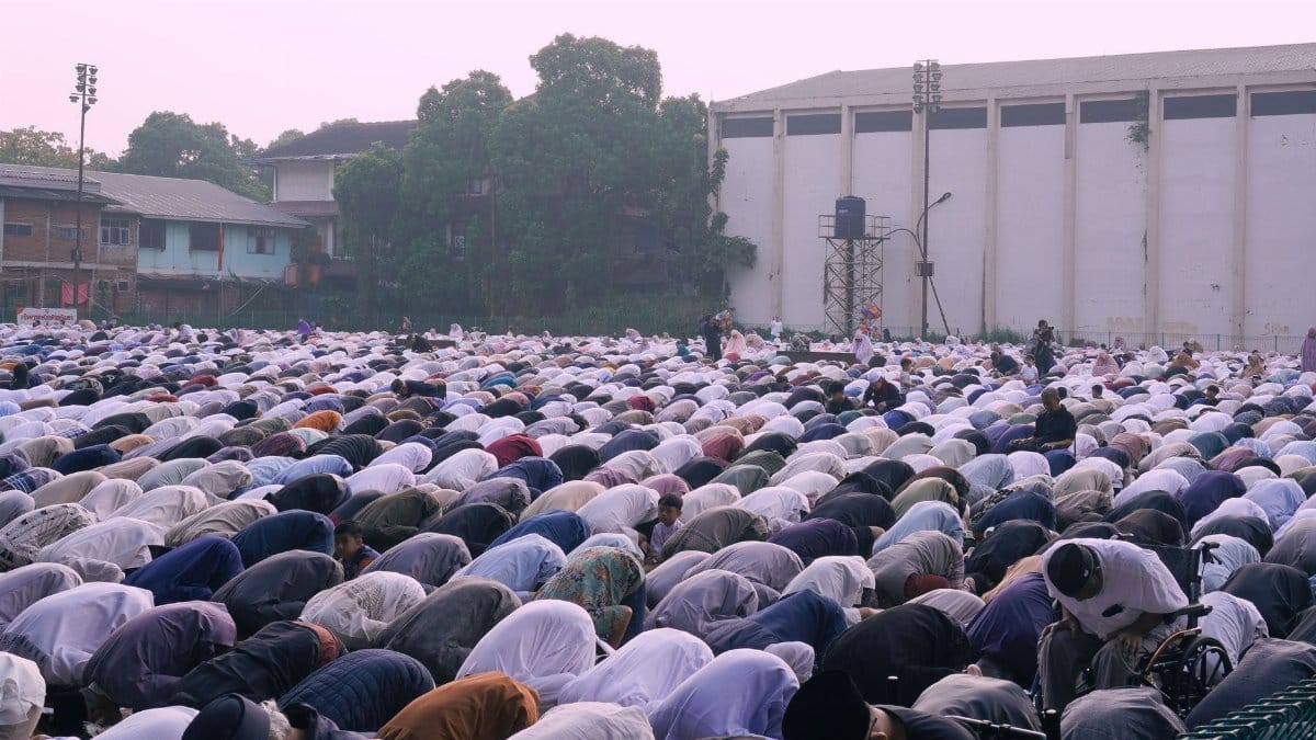 Large group of people gathered outdoors for prayer at dusk. Community, faith, and tradition are highlighted.