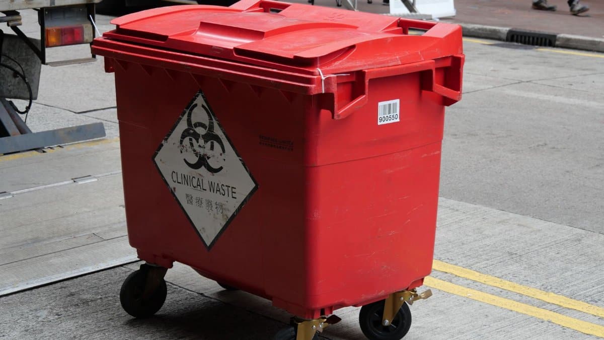 A red clinical waste bin labeled with biohazard symbol on a city street indicating proper waste management.