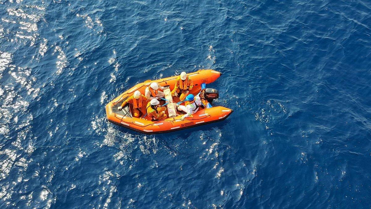 Safety crew on an orange inflatable rescue boat navigating the open sea.