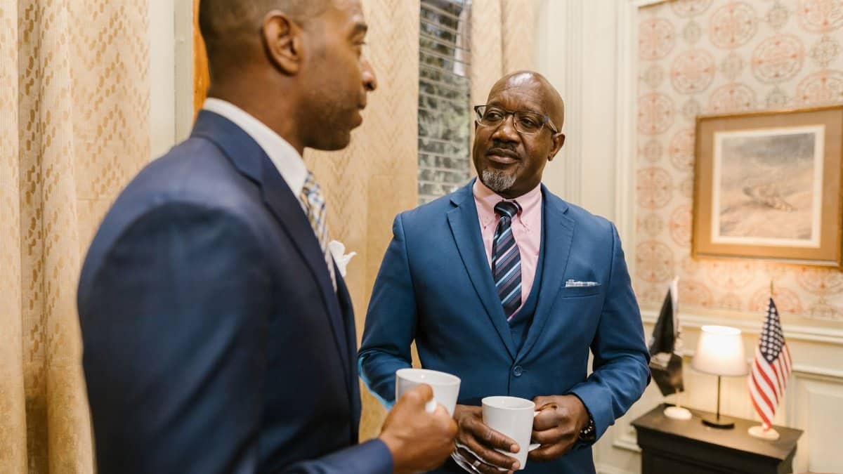 Two businessmen in suits having a coffee break and discussing business indoors.