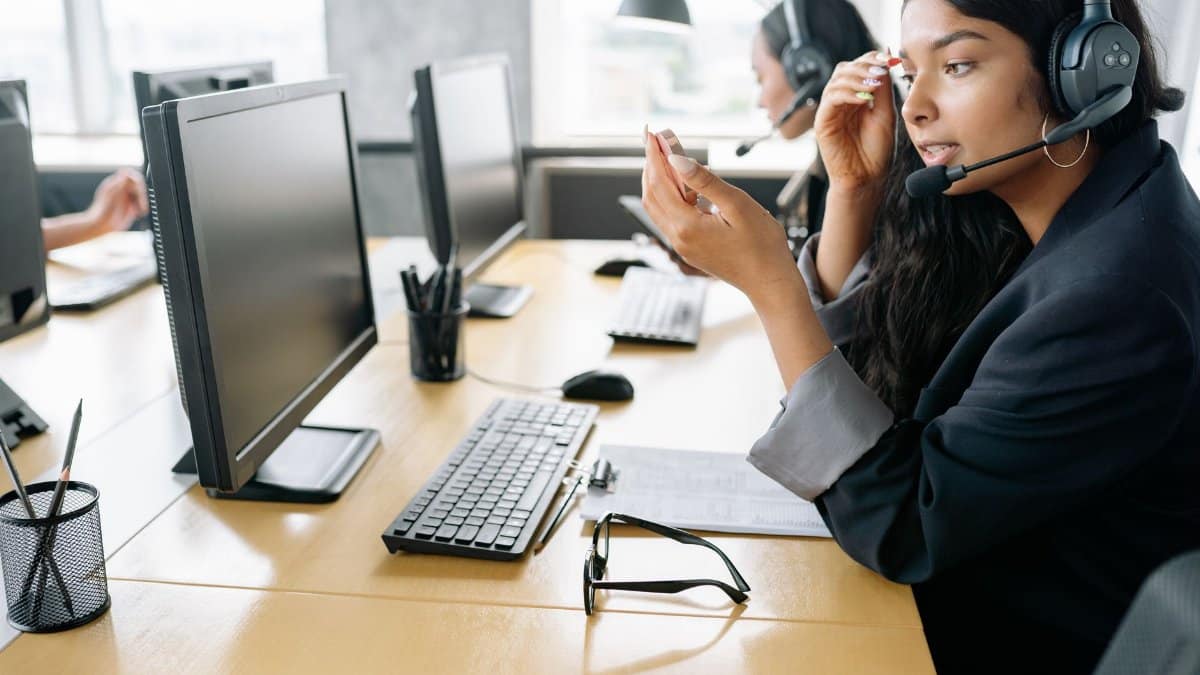 South Asian woman providing customer support in a modern office environment, equipped with a headset.