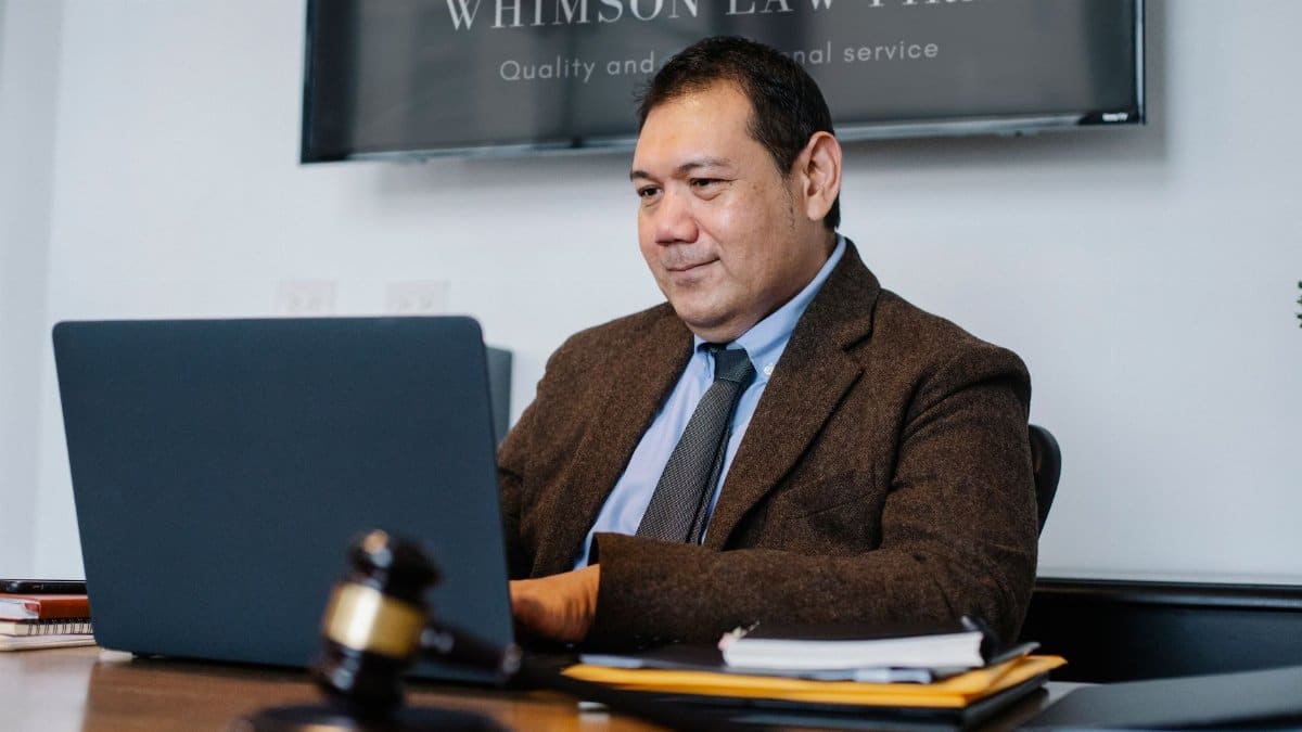 Experienced middle aged ethnic happy male working with netbook at table with judge hammer
