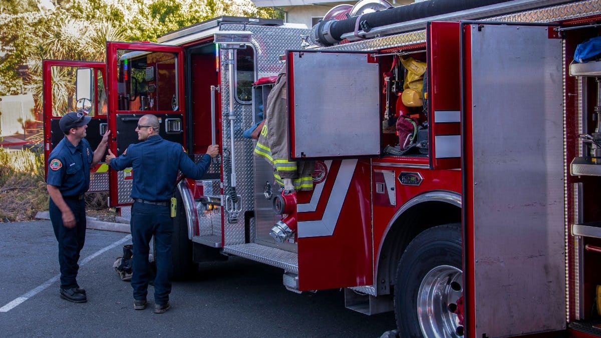 Firefighters inspect and prepare equipment on a fire truck outside the station.