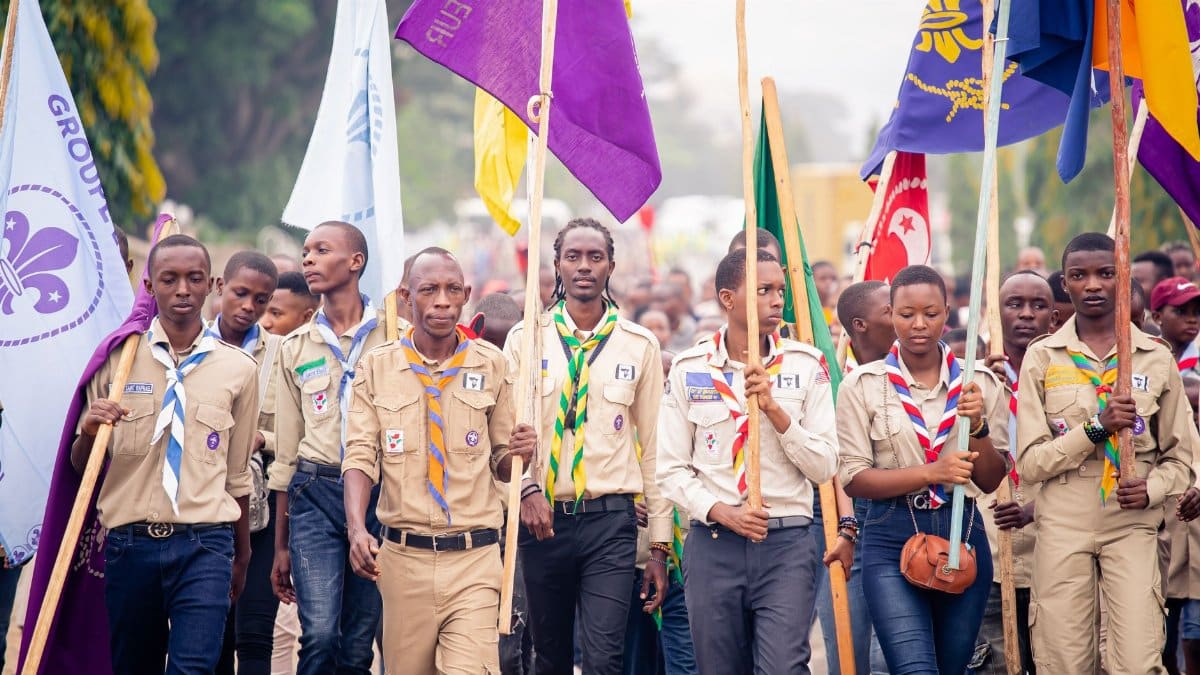 A group of scouts proudly marching in a parade, showcasing colorful flags and uniforms.
