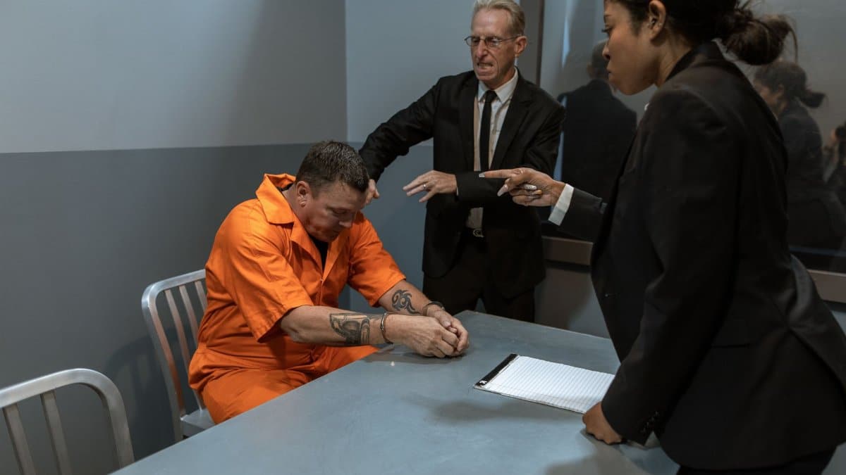 A tense interrogation scene with officers and a prisoner in an orange jumpsuit.