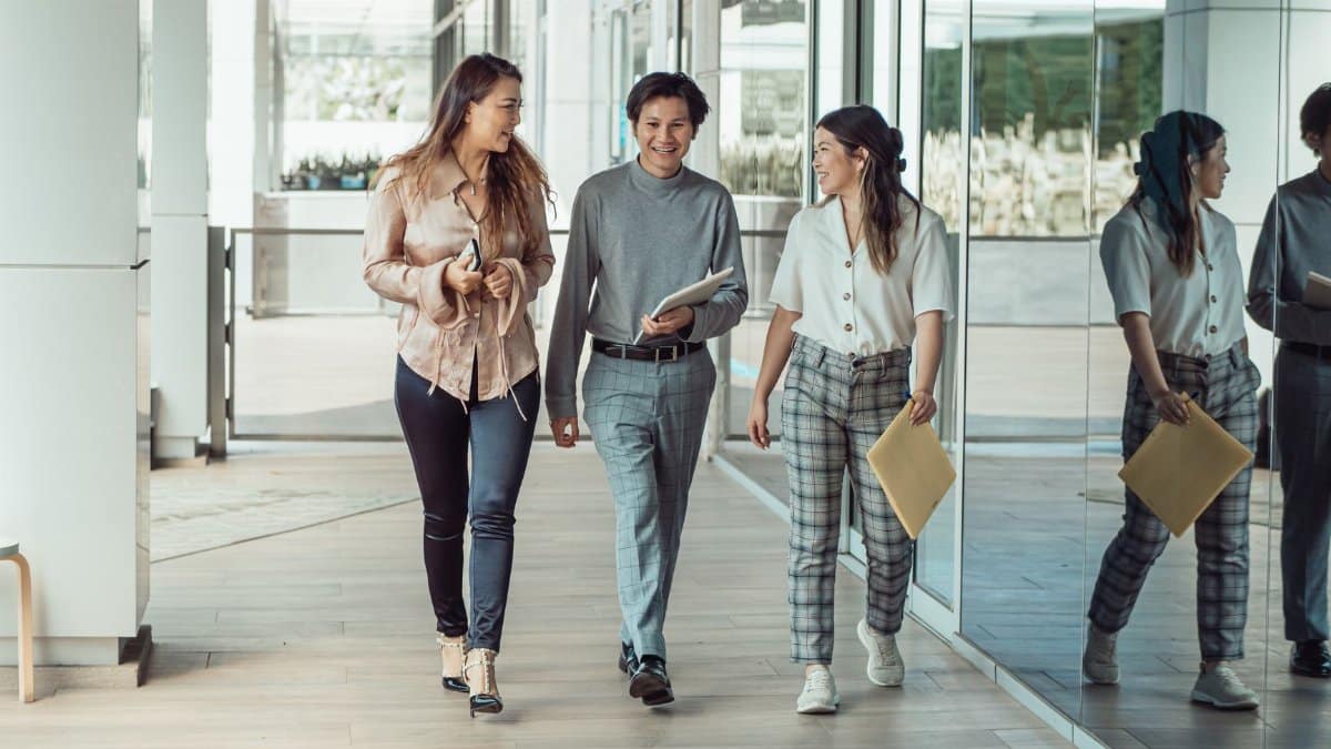 Three colleagues walking and conversing in a modern office, reflecting teamwork and collaboration.