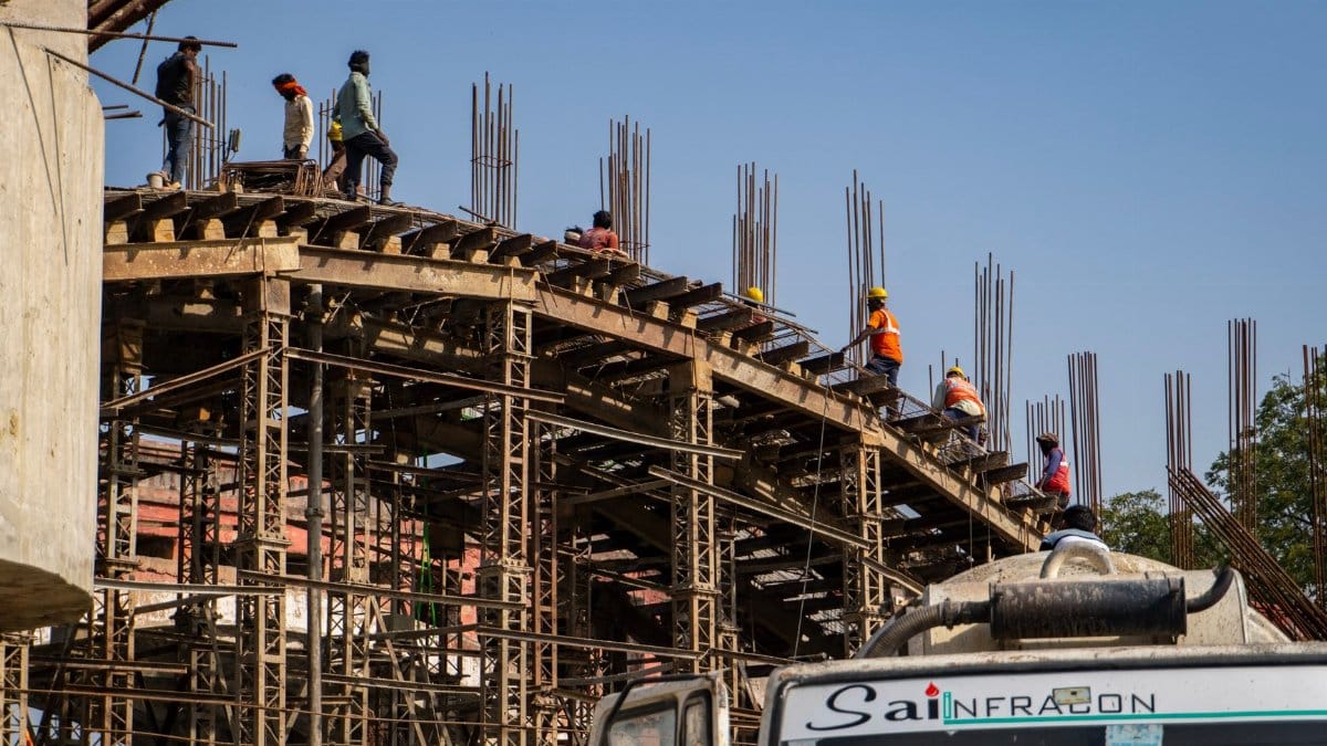 Workers construct a large industrial structure under clear blue skies, wearing safety gear.