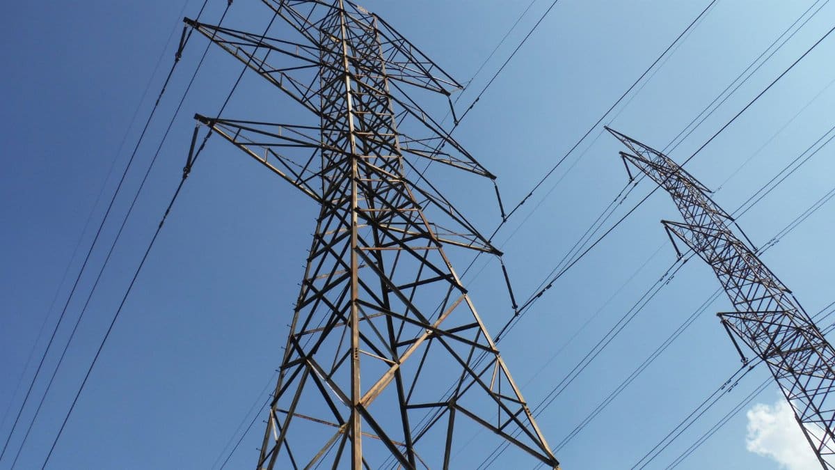 Low angle view of towering electrical transmission lines and pylons under a clear blue sky, conveying energy and electricity concepts.