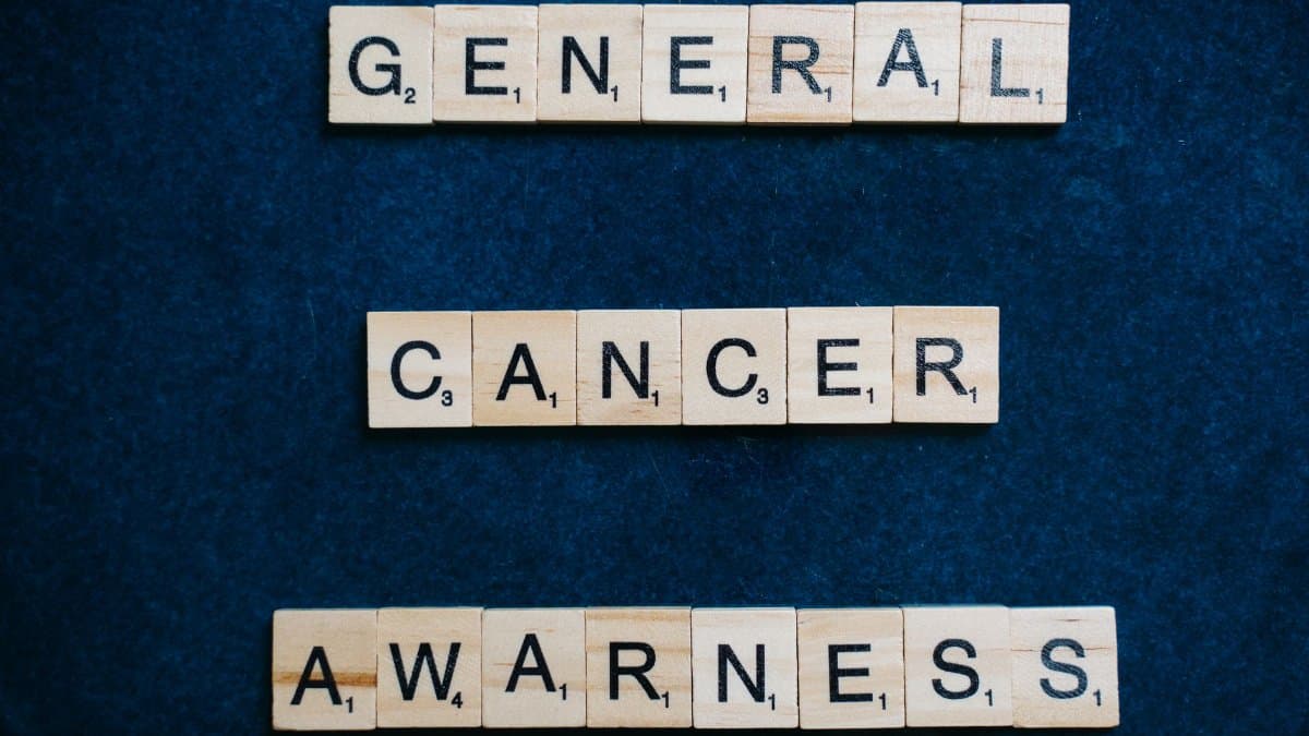 Words 'General Cancer Awareness' spelled with Scrabble tiles on a blue surface, promoting awareness.