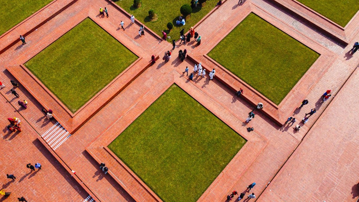 Aerial shot of a geometric public square with grass and people walking on red brick paths.