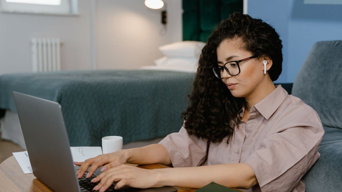 A woman focusing on remote work in a comfortable bedroom with modern decor and laptop.
