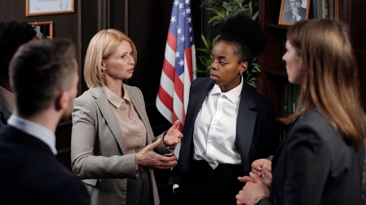 Diverse group of professionals in a discussion in a formal setting with an American flag.