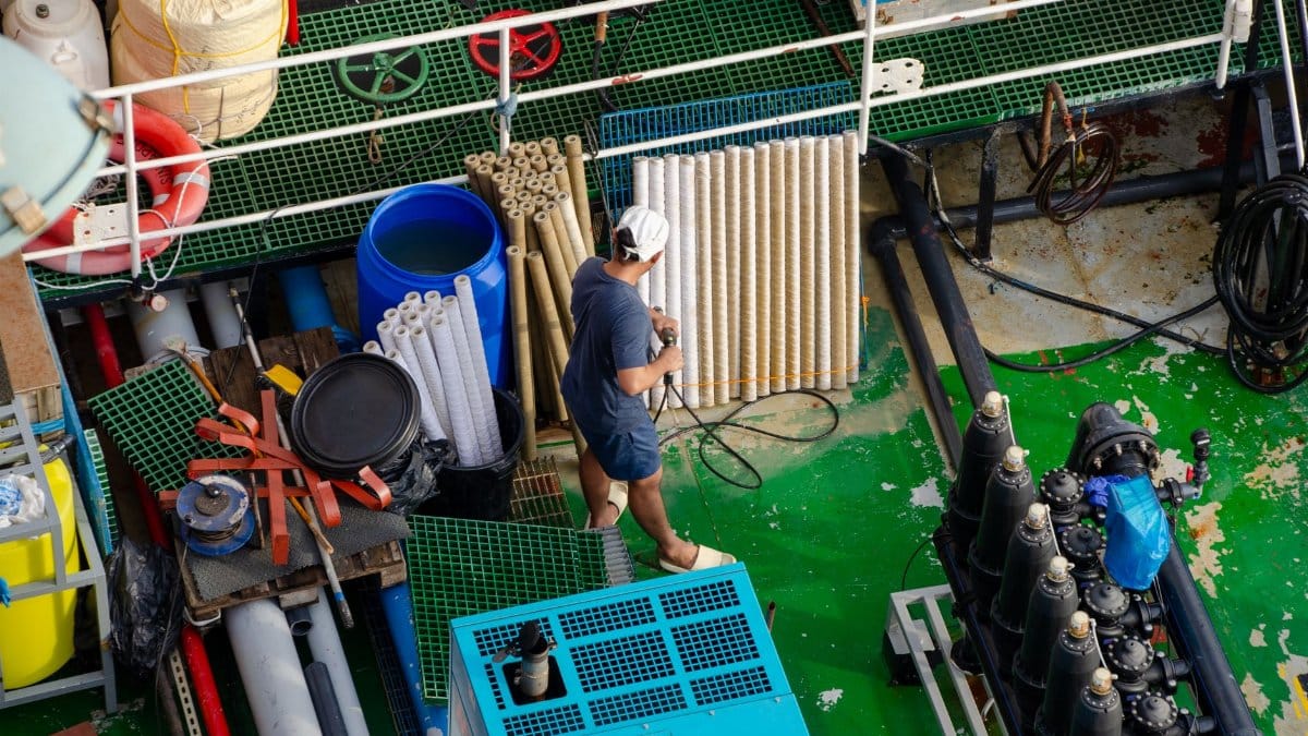 Aerial view of a worker on a ship deck managing industrial equipment and pipes.