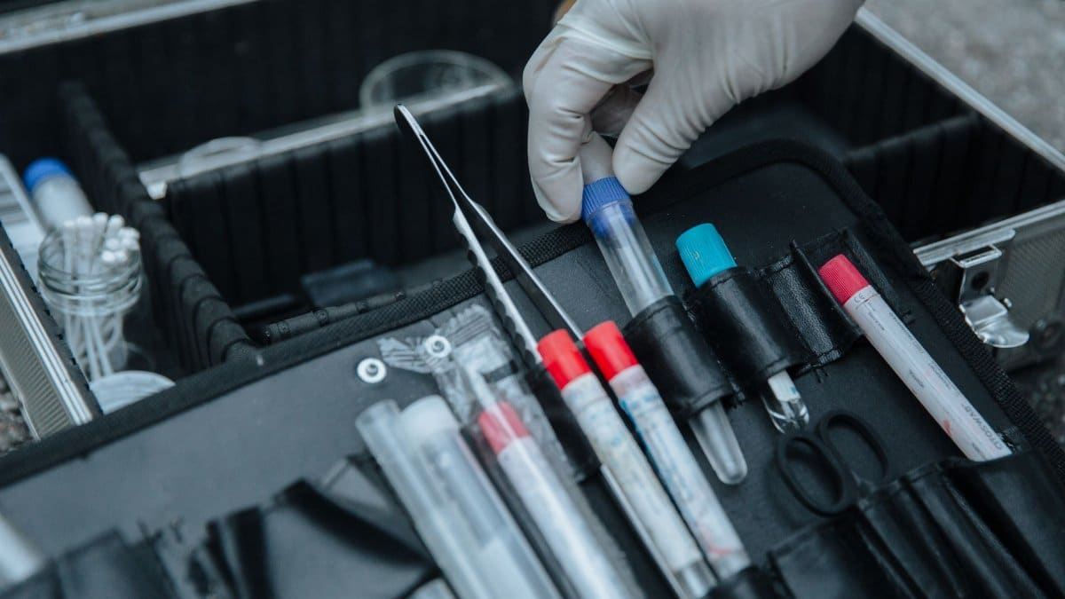 Gloved hand handling test tube in forensic equipment case at crime scene.