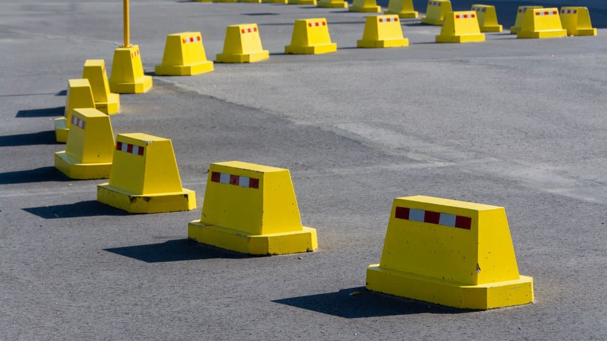 A row of bright yellow traffic barricades on a sunny asphalt road.