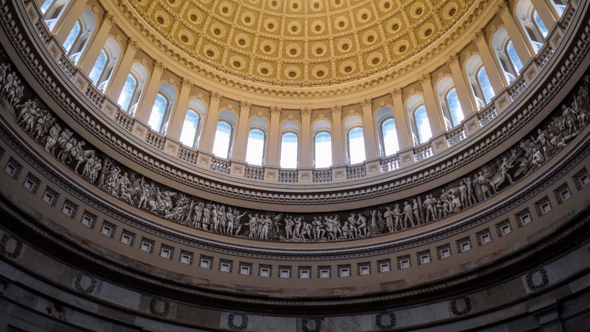 From below of carved stone bas relief frieze and arched windows decorating dome of United States Capitol located in Washington DC