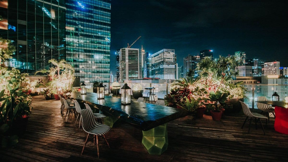 A vibrant rooftop garden with seating overlooking an illuminated cityscape at night.