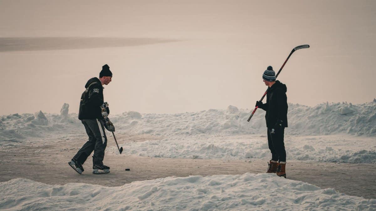 Two teenagers enjoy a game of ice hockey on a frozen lake during a winter day.