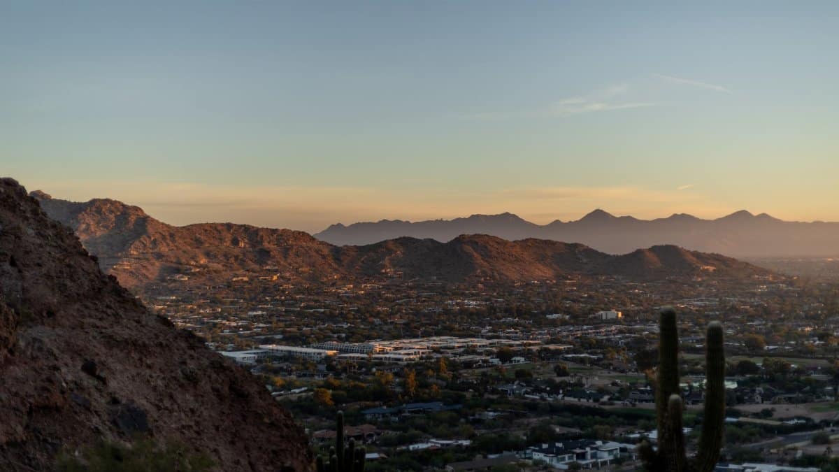 Breathtaking view of Phoenix cityscape and desert mountains at sunset with silhouetted cacti.