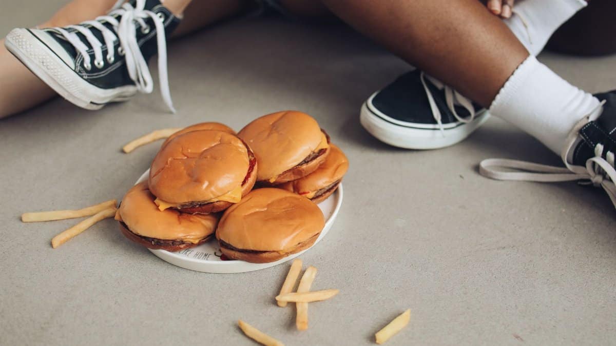 A casual meal with burgers and fries on the floor, surrounded by sneakers.