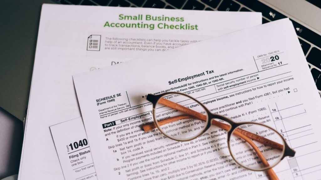 Close-up of tax forms and a small business accounting checklist on a laptop.