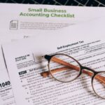 Close-up of tax forms and a small business accounting checklist on a laptop.