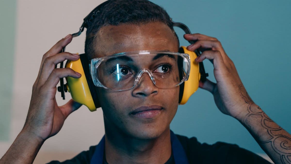 Portrait of a young engineer adjusting ear protection and safety glasses, showing focus and preparation indoors.