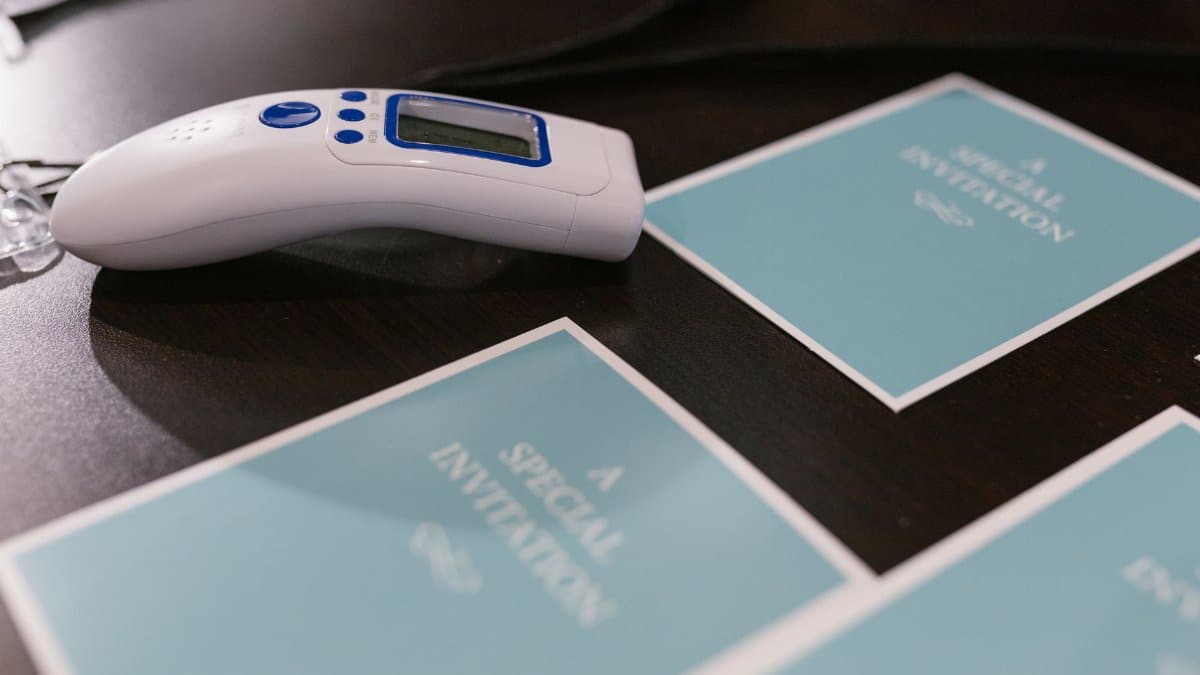 A close-up view of invitations and an infrared thermometer on a wooden surface, symbolizing event preparation and safety.