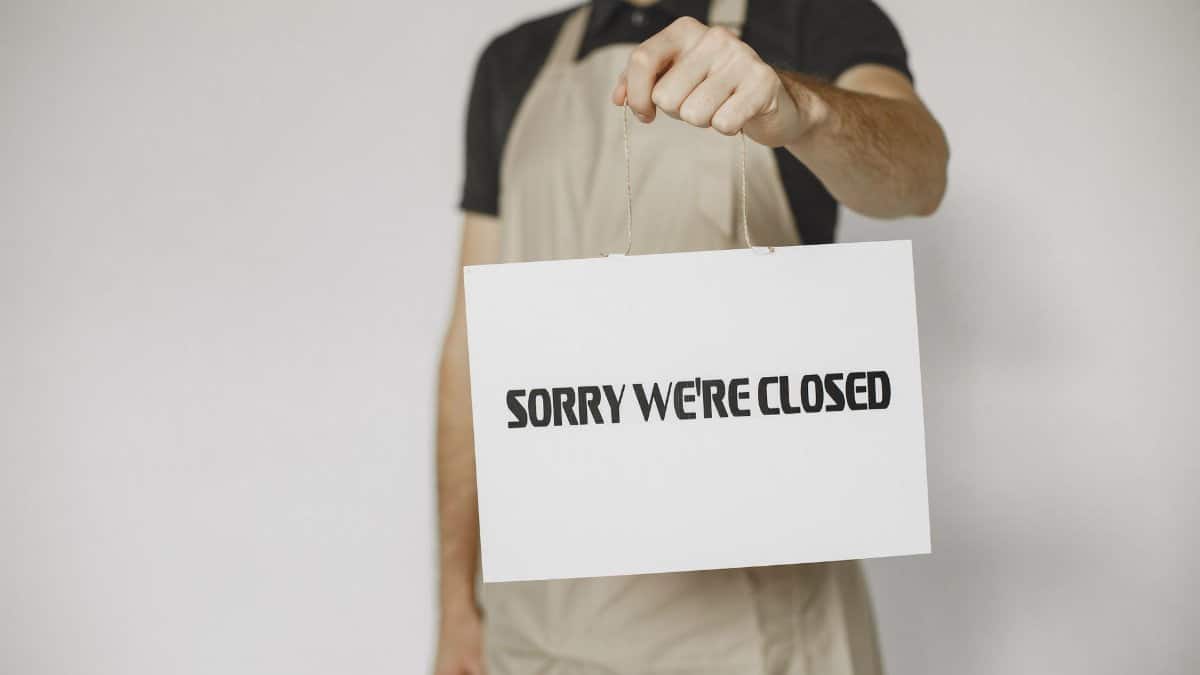 Close-up of a man holding a 'Sorry We're Closed' sign, ideal for business or retail concepts.