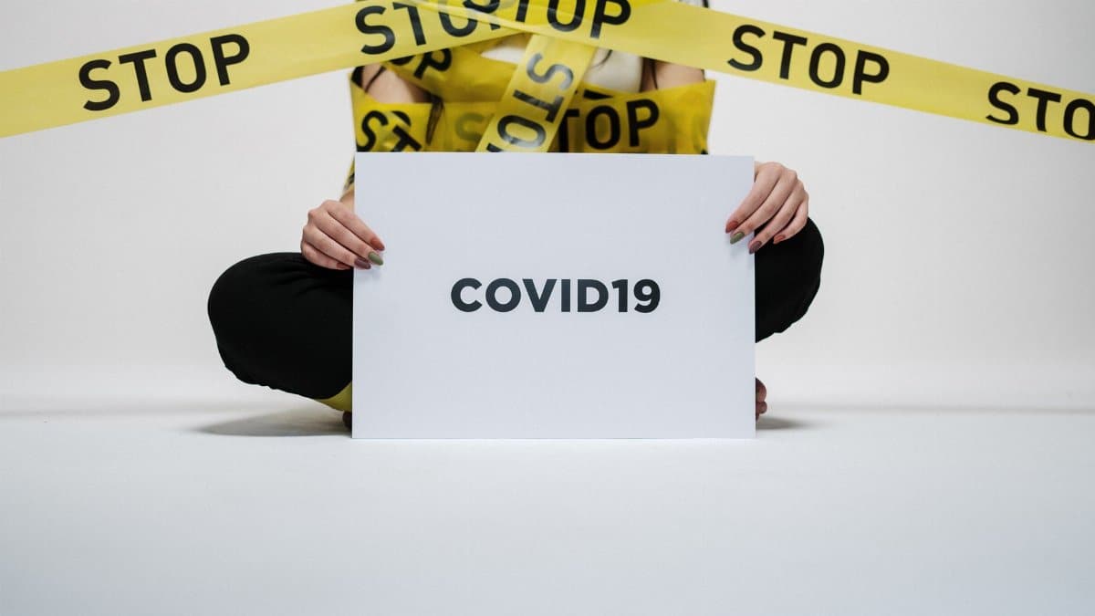 Person holding COVID-19 sign surrounded by yellow stop tape, symbolizing quarantine and safety.