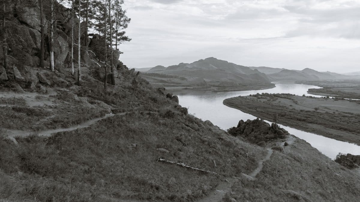 Black and white of mounts with grass and narrow paths against wavy river in daytime