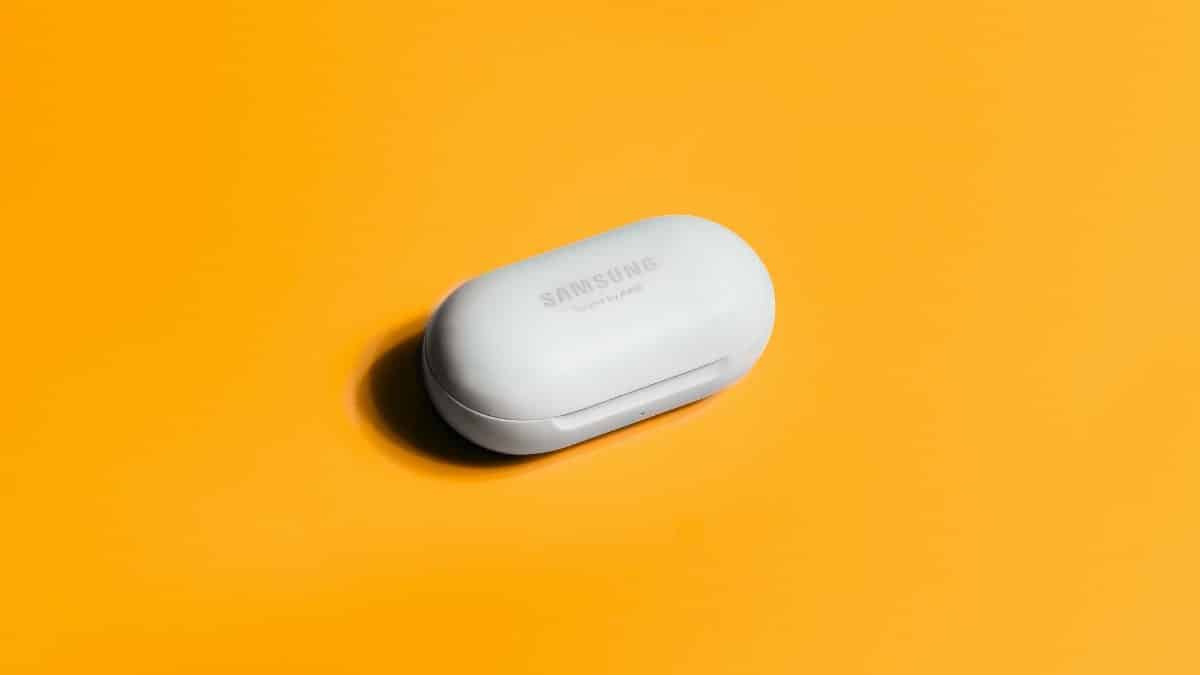 White Samsung wireless earbuds case on a bright yellow background, showcasing sleek tech design.