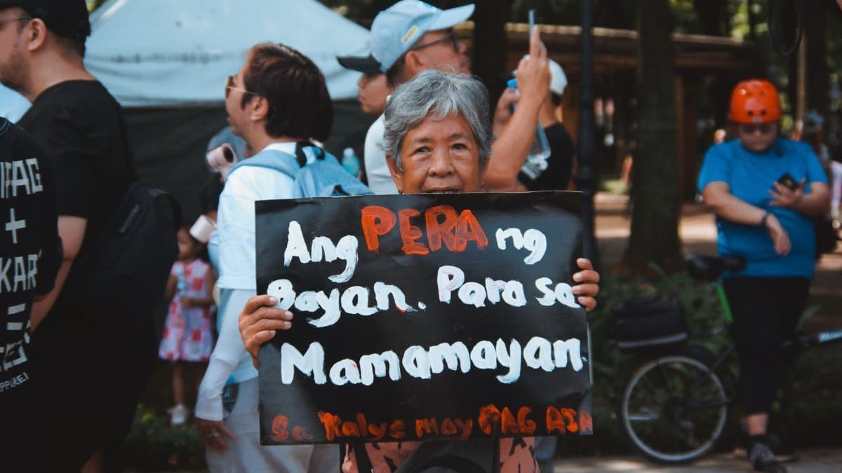 A protest scene with diverse participants holding a sign expressing a political message outdoors.