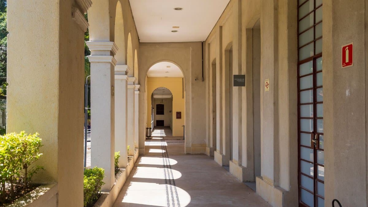 Sunlit corridor with archways casting shadows on a sunny day.