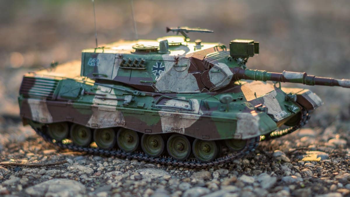 Detailed close-up of a model military tank with camouflage, displayed on rocky outdoor terrain.