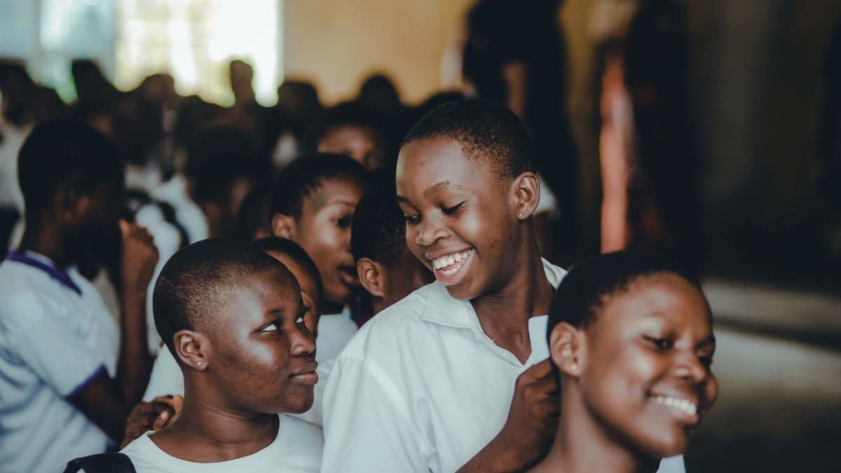 A group of African teenagers in school uniforms smiling and interacting indoors.
