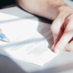 Hands signing a contract with a blue pen, close-up view.