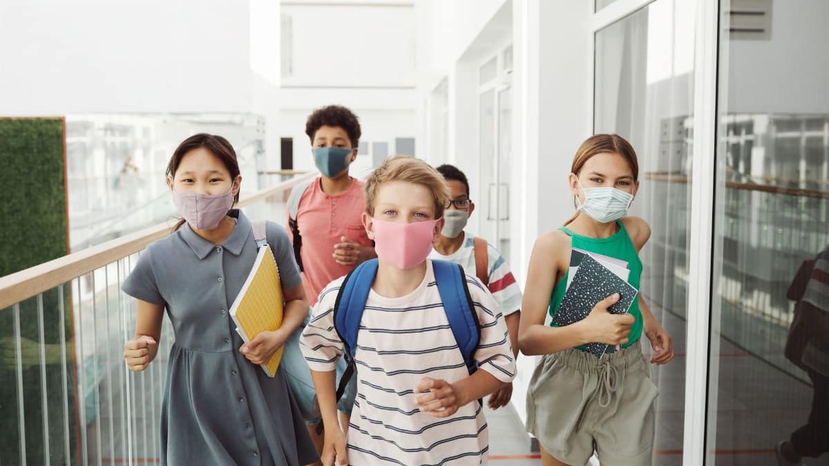 Group of diverse teenagers wearing face masks and holding notebooks, adapting to new norms in education.