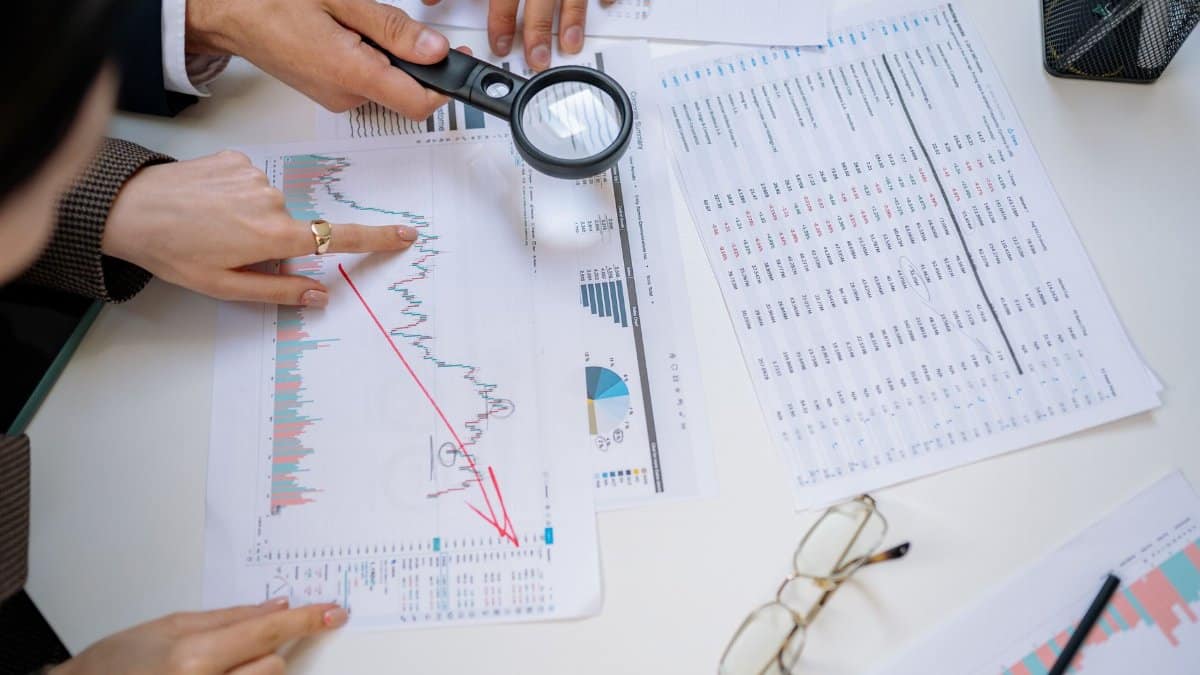 Business professionals examining financial documents with magnifying glass for detailed analysis.