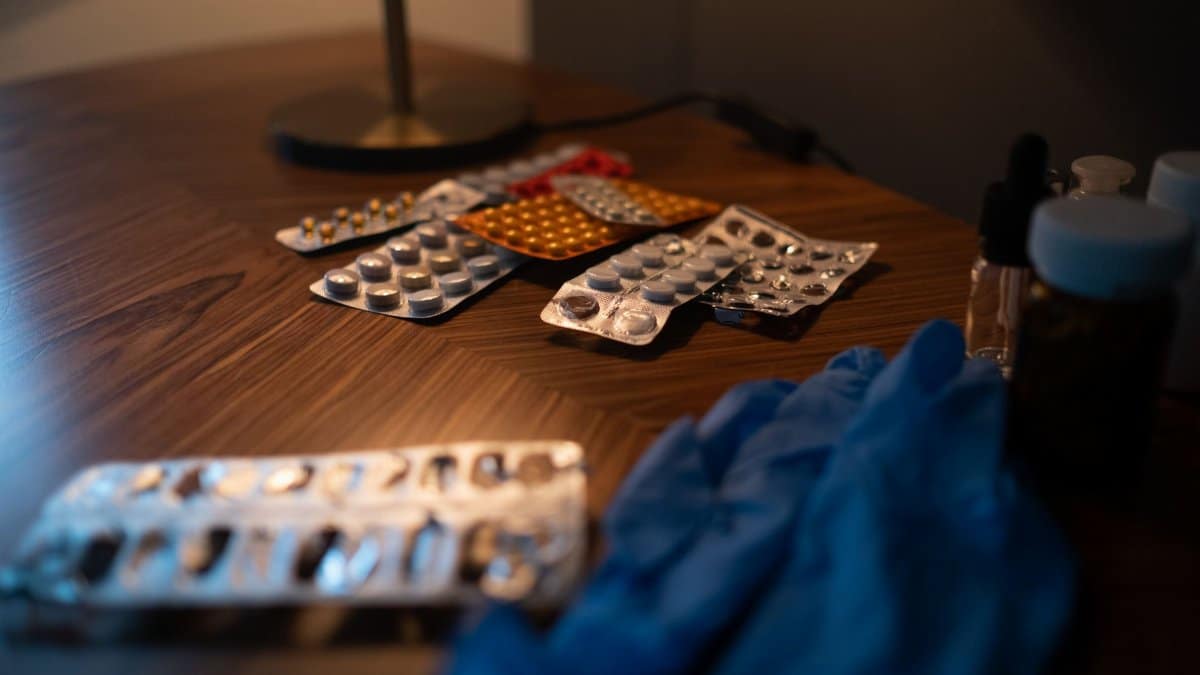 Close-up of various medication blister packs and gloves on a wooden table, signifying health and recovery.