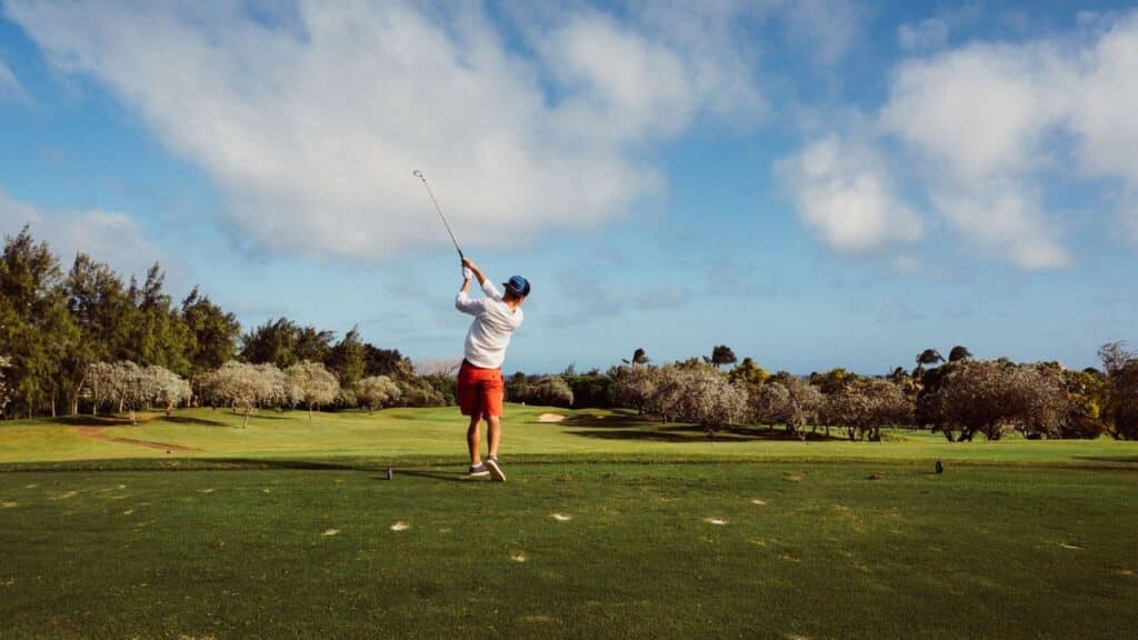 A golfer swings on a picturesque golf course with lush greenery and a clear blue sky, epitomizing outdoor leisure.