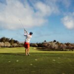 A golfer swings on a picturesque golf course with lush greenery and a clear blue sky, epitomizing outdoor leisure.