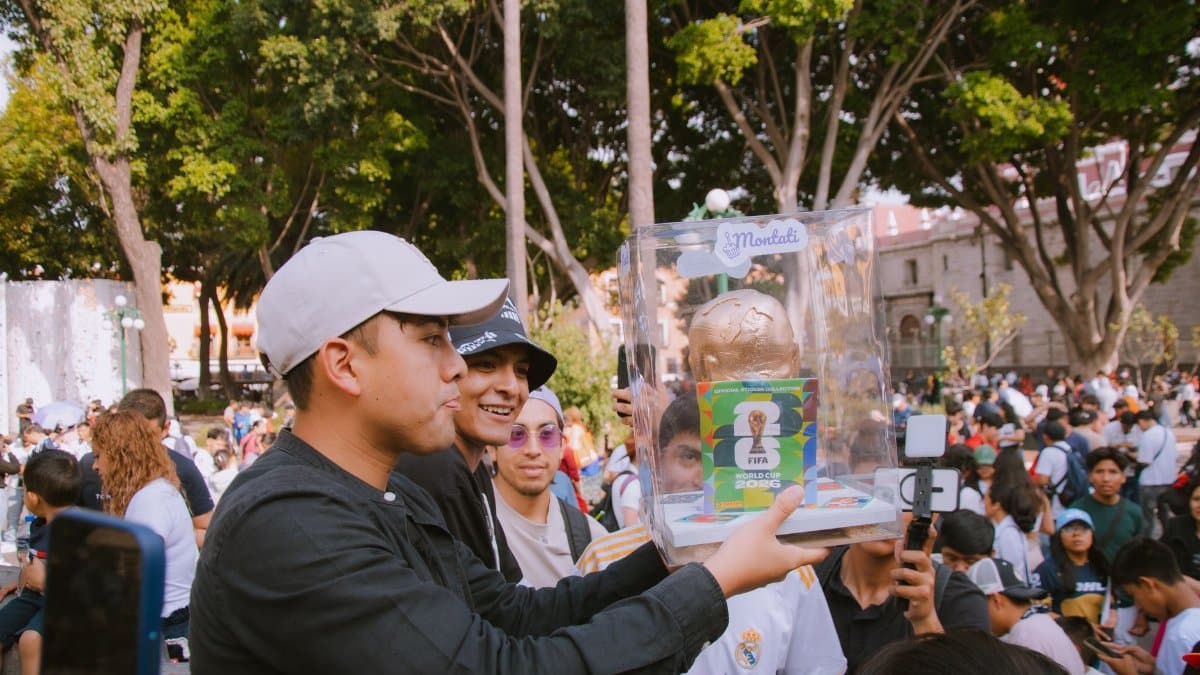 Group of people celebrating with a FIFA World Cup trophy replica in a vibrant outdoor setting.