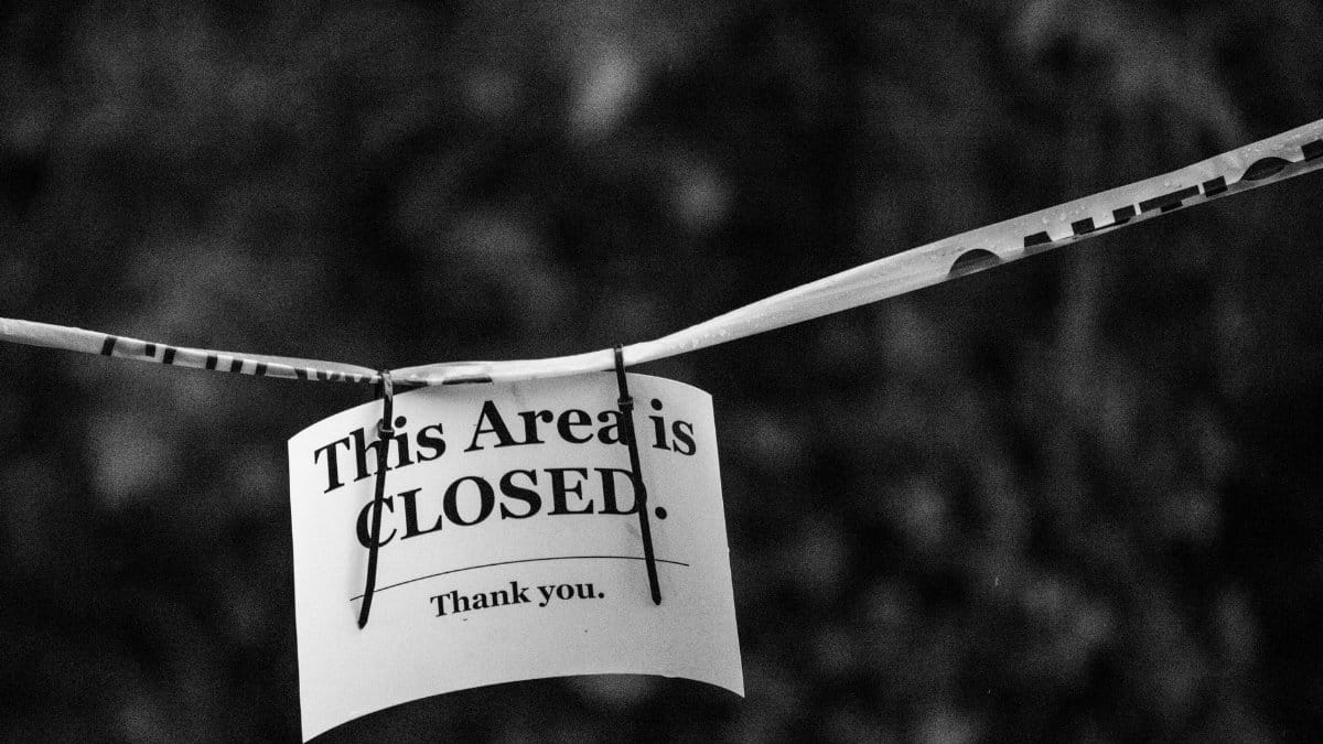 A black and white photo of a sign reading 'This Area is CLOSED.' in a blurred outdoor setting.