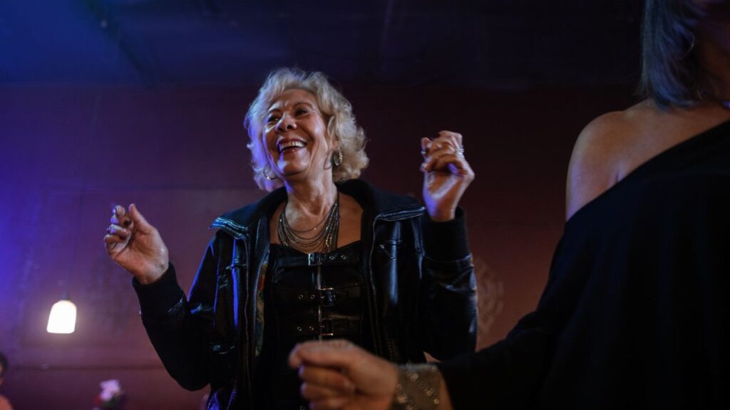 Senior woman wearing a black leather jacket enjoying a fun night out dancing at a club.